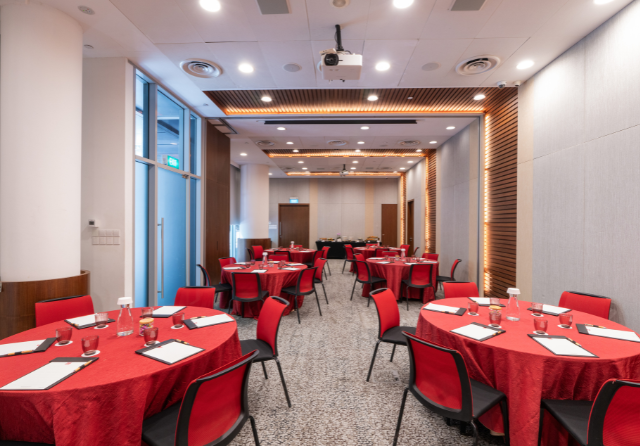Cluster meeting setup in a modern function room at ibis Singapore on Bencoolen featuring round tables with red tablecloths, meeting stationery, projector facilities and warm ambient lighting