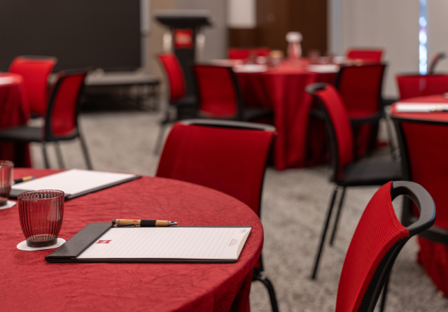 Close-up of a cluster meeting setup at ibis Singapore on Bencoolen featuring round tables with red tablecloths, meeting notepads, pens and modern red chairs in a corporate event space