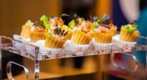 Elegant golden pastry cups filled with fresh seafood, vibrant greens, and delicate edible flowers, presented on a modern acrylic stand.