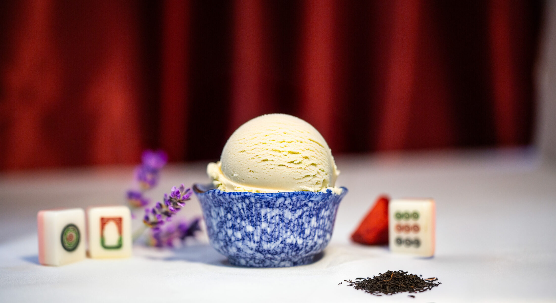 A scoop of Earl Grey lavender ice cream in a blue marble bowl, with lavender sprigs, tea leaves, and mahjong tiles.