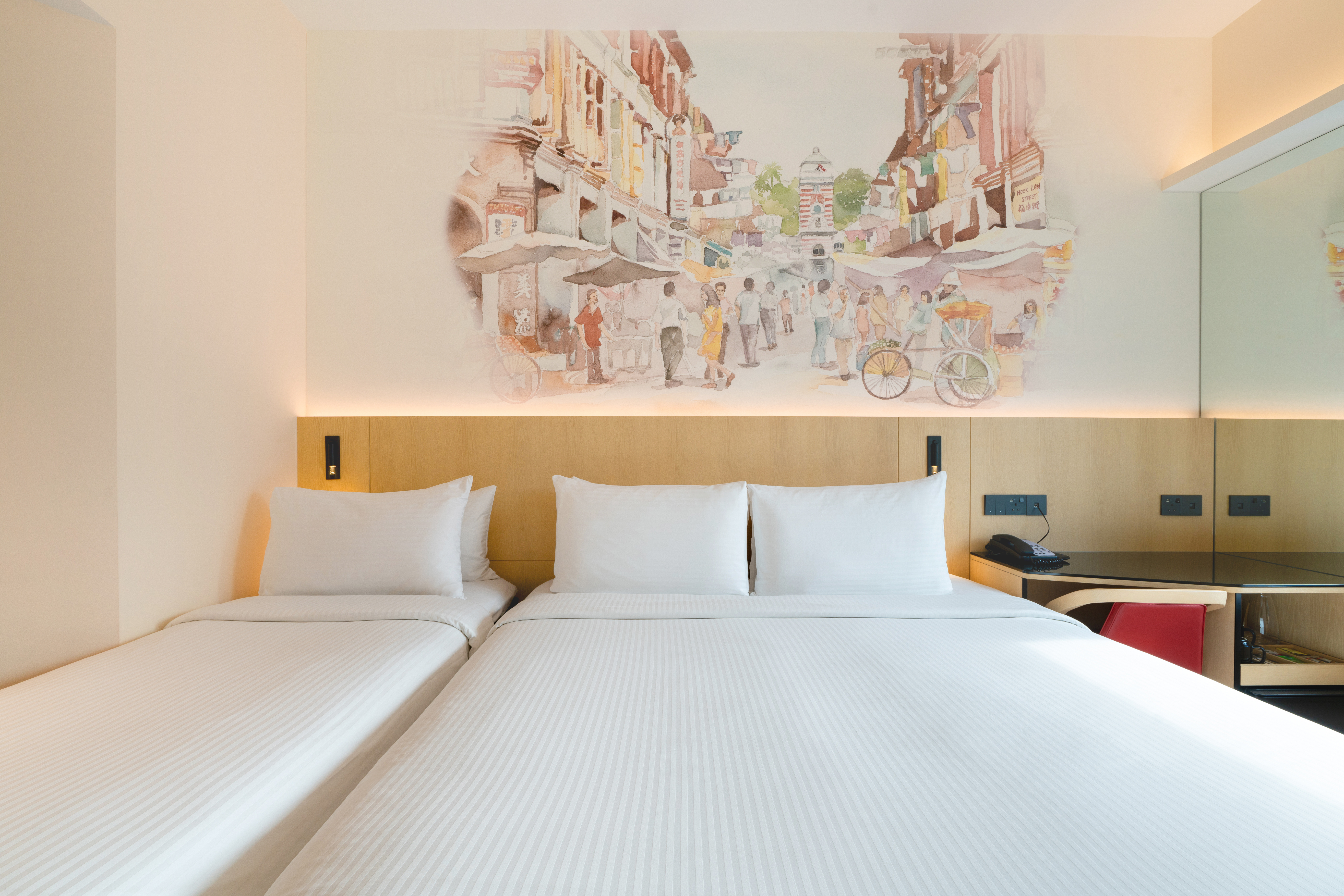 Hotel room featuring 1 Queen bed and 1 single bed with a decorative headboard mural illustrating a olden day Singapore street at the background, a study table, and a bay window offering natural light.