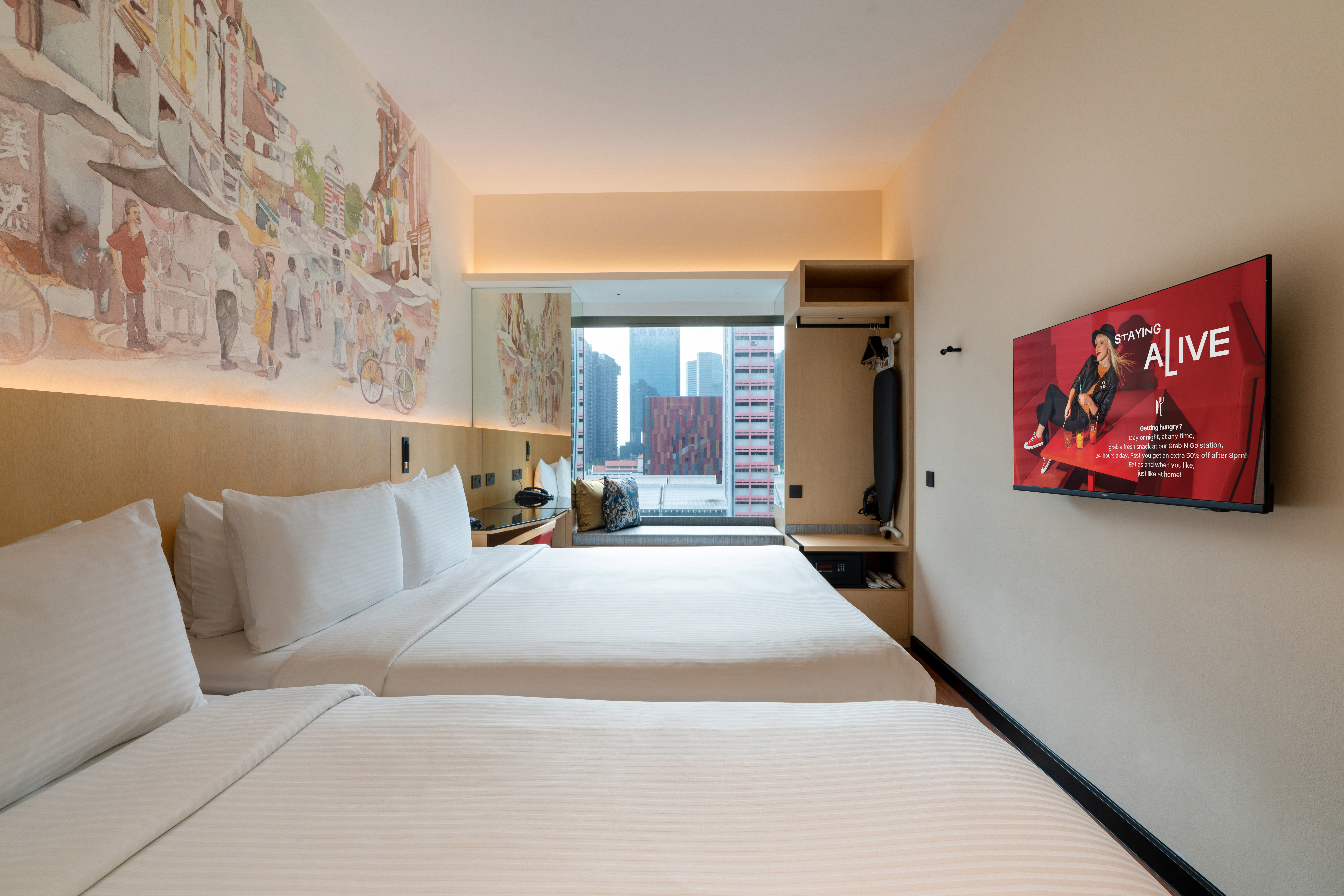 Hotel room featuring 1 Queen bed and 1 single bed with a decorative headboard mural illustrating a olden day Singapore street at the background, a study table, and a bay window offering natural light.