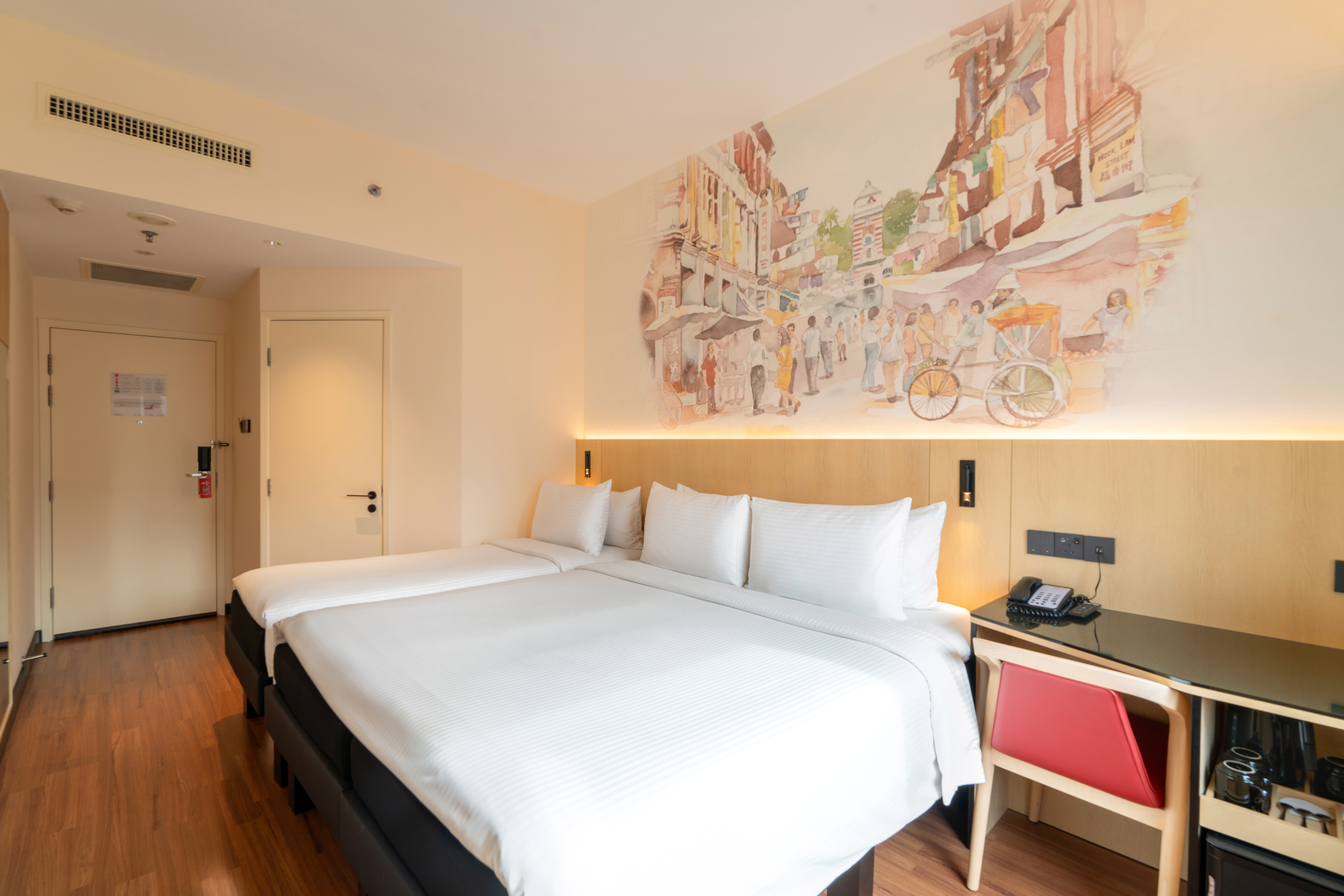 Hotel room featuring 1 Queen bed and 1 single bed with a decorative headboard mural illustrating a olden day Singapore street at the background, a study table, and a bay window offering natural light.