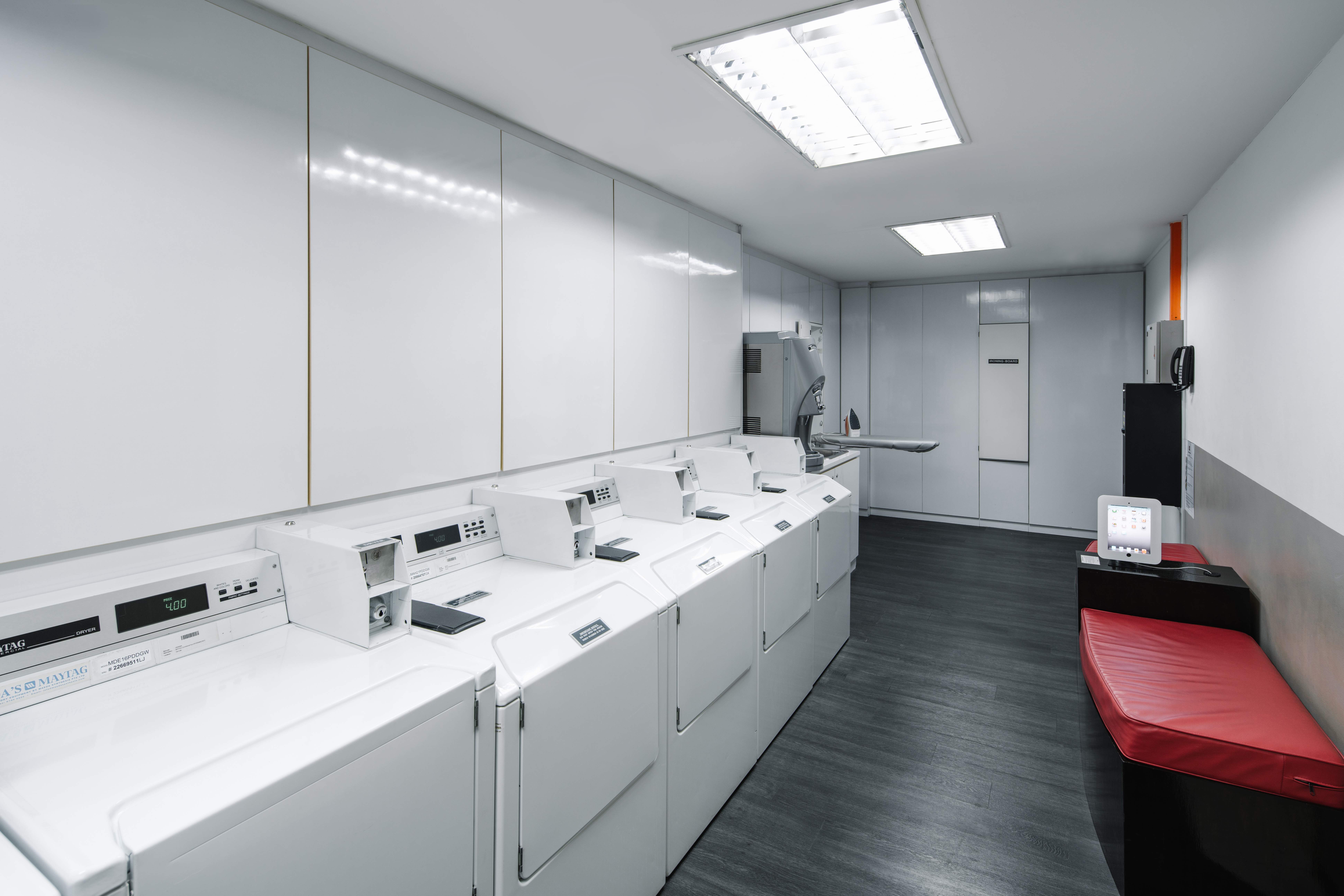 Modern hotel laundrette room with multiple washing machines, dryers, and a seating area.