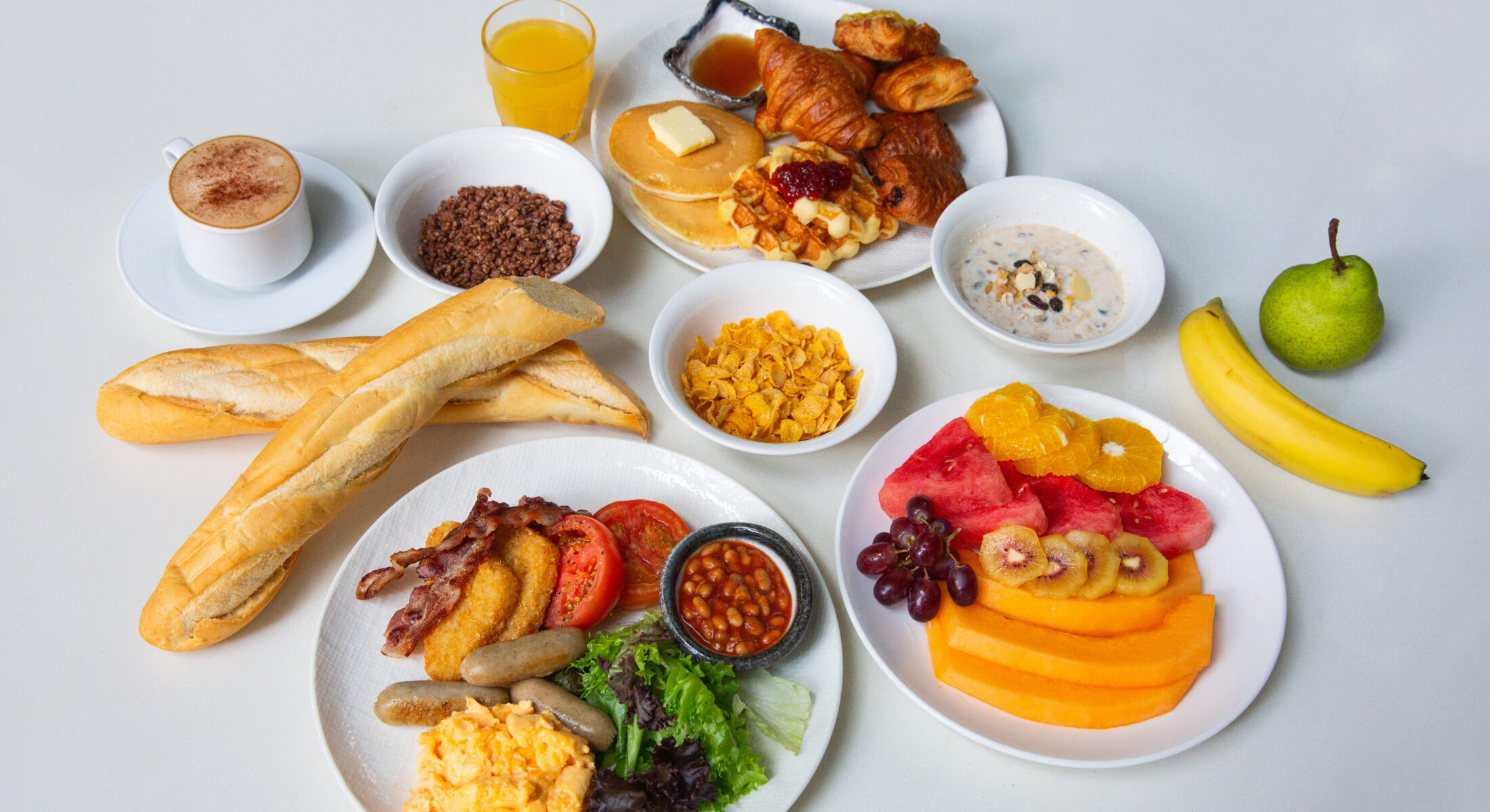 Continental breakfast with baguettes, pastries, cereals, fruits, and juice.