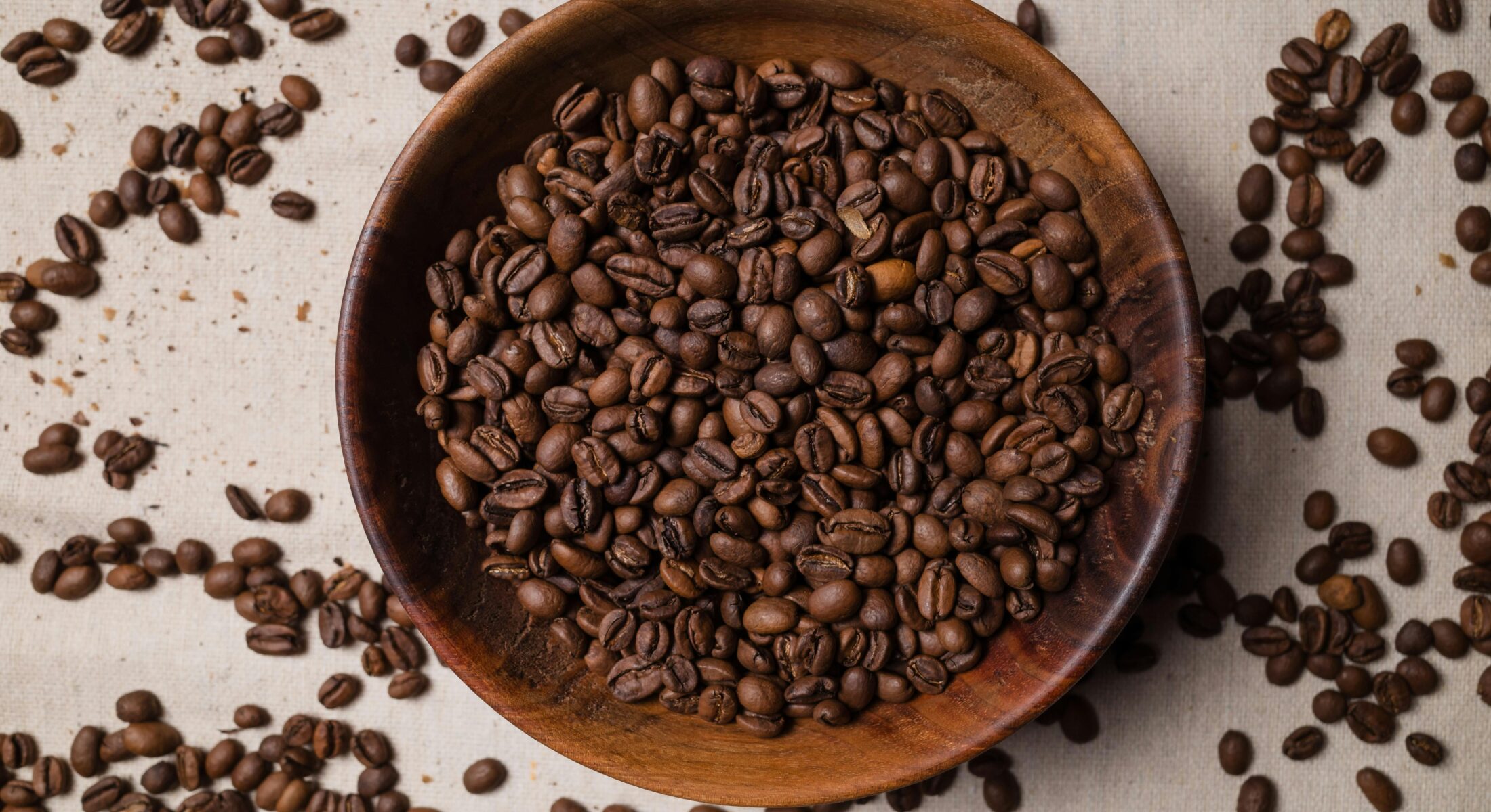 Close-up of roasted coffee beans in a wooden bowl with scattered beans on a fabric surface, symbolizing the vibrant food and beverage culture showcased at FHA 2026.