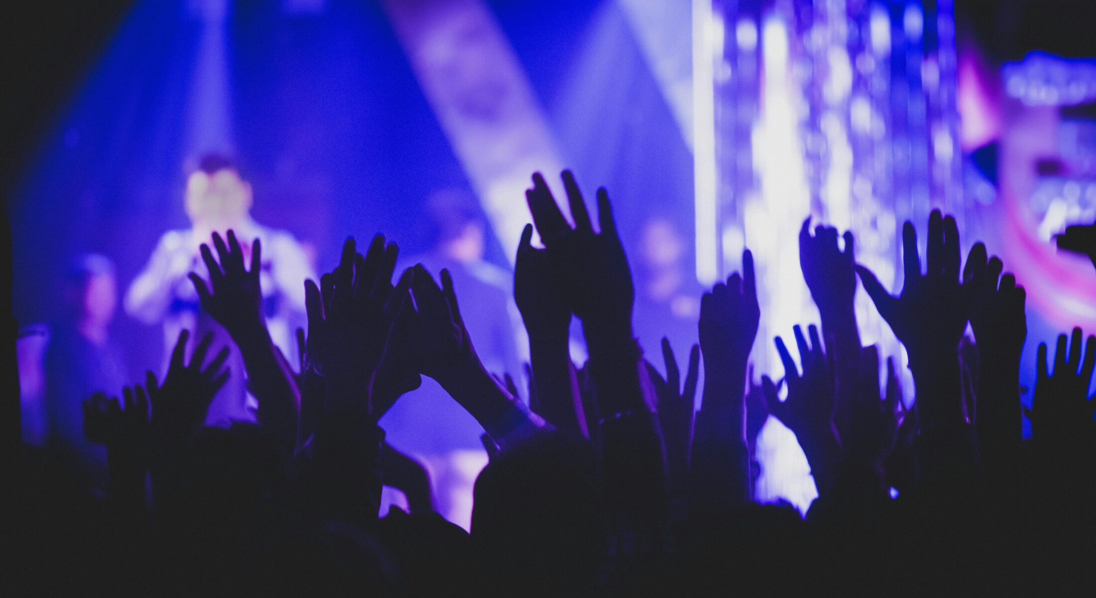 Concert crowd with raised hands under vibrant stage lights, capturing the excitement of live K-pop performances during the BTS World Tour in Singapore.