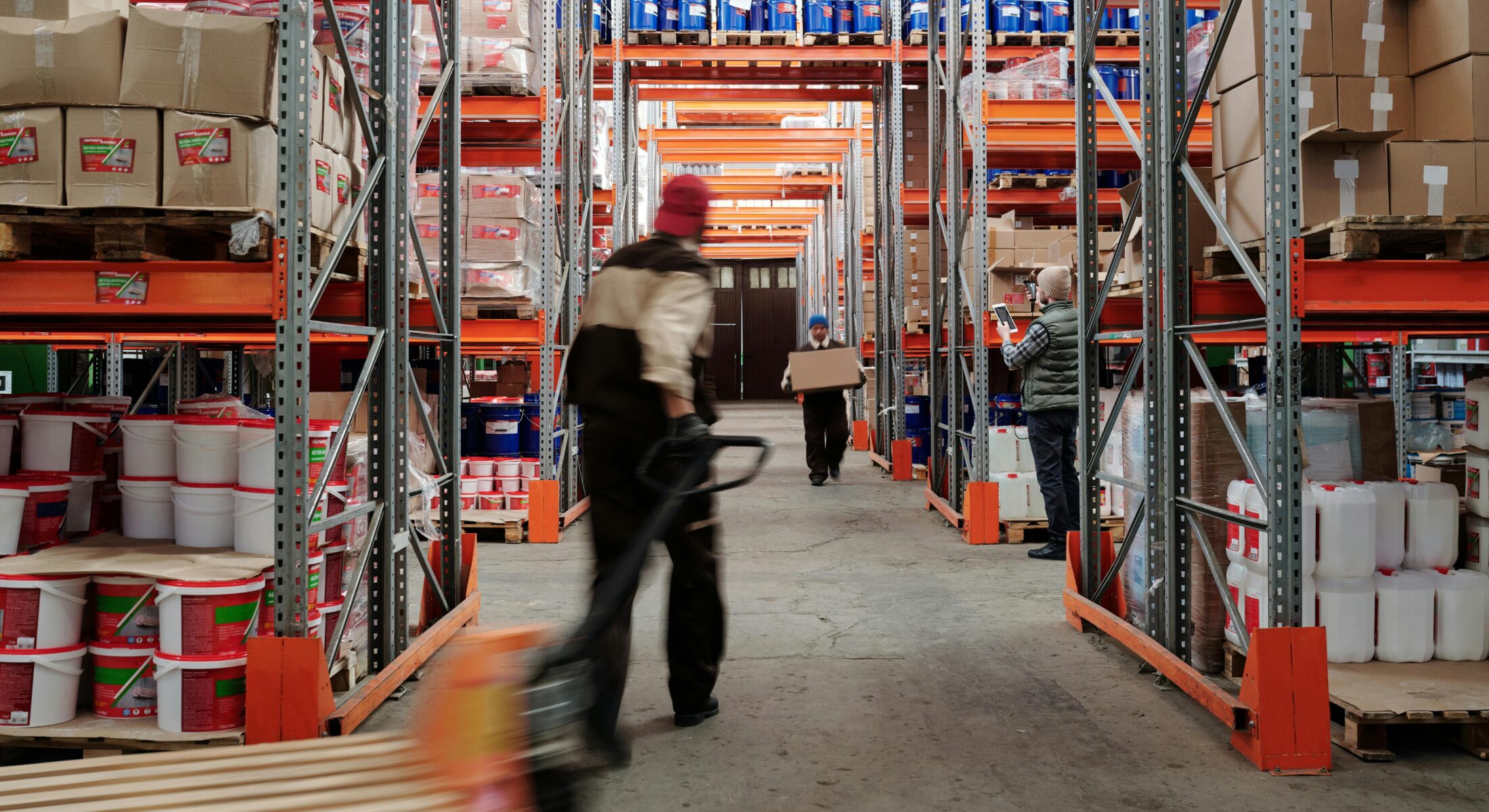 Warehouse workers moving goods through aisles of racked inventory in a large logistics facility.