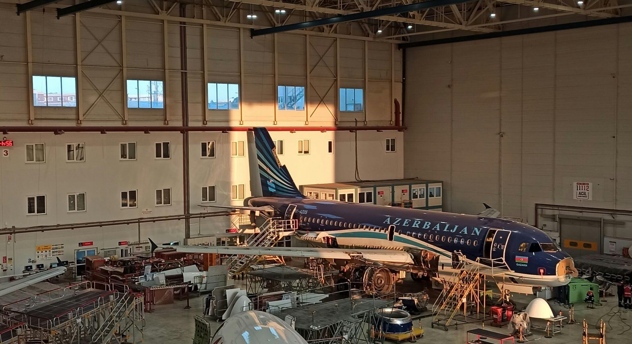 Wide view of aircraft undergoing maintenance inside a large aviation hangar with engineers, scaffolding and equipment.