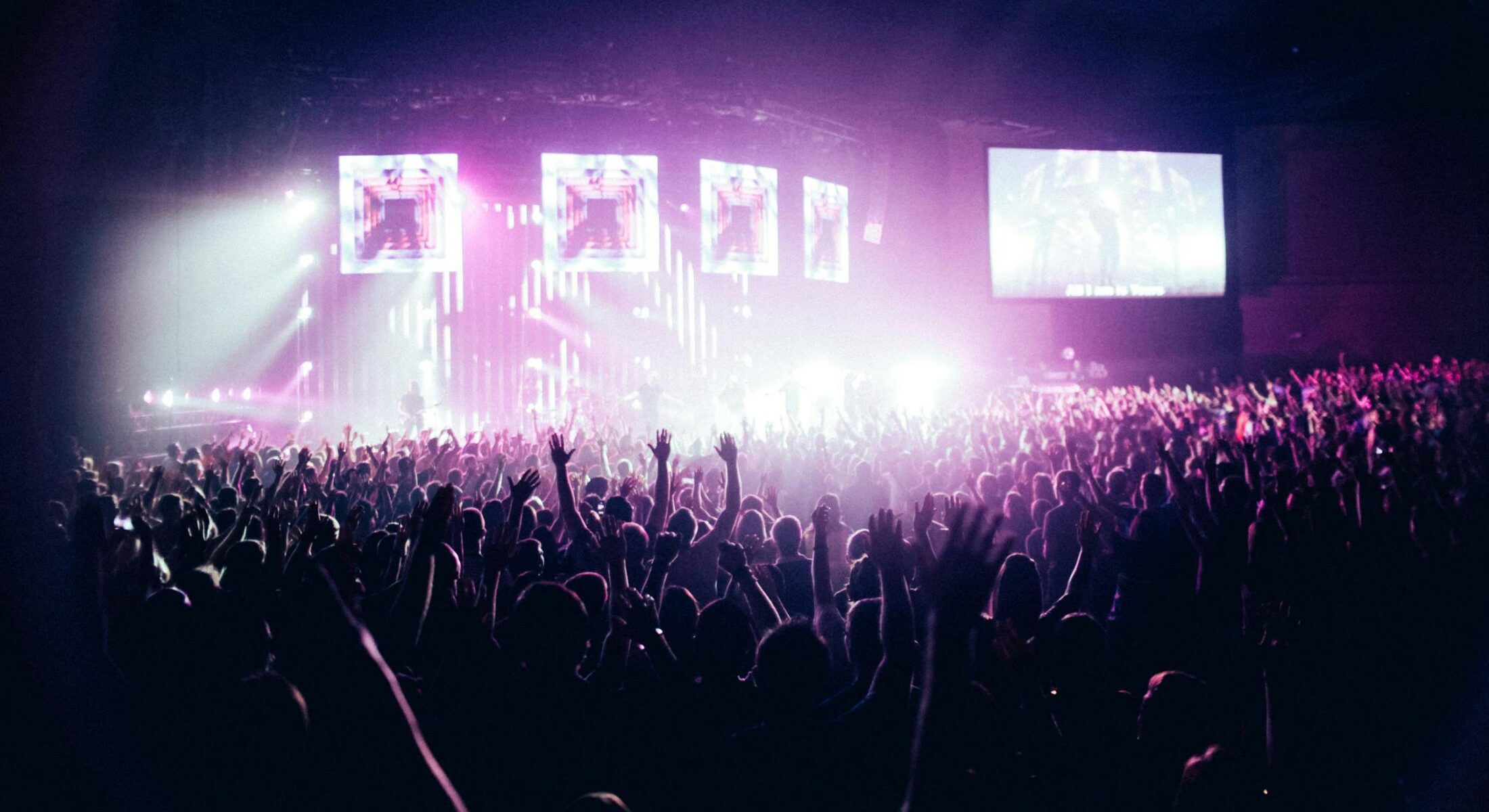 Large crowd at a stadium concert with raised hands, vibrant stage lighting and screens during a live music performance in Singapore