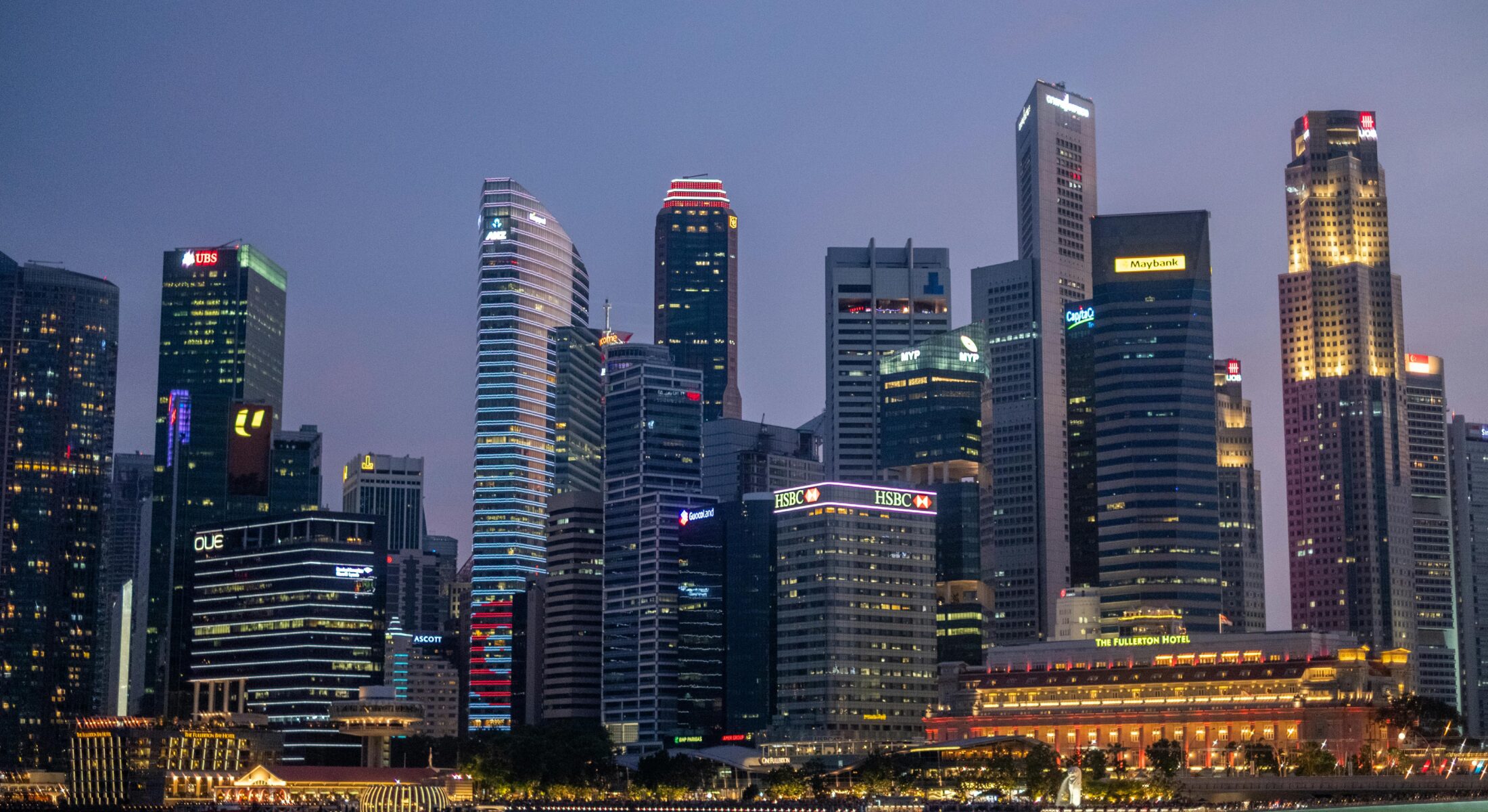 Evening skyline of the Singapore Central Business District, featuring major office towers along Marina Bay and the Singapore River.