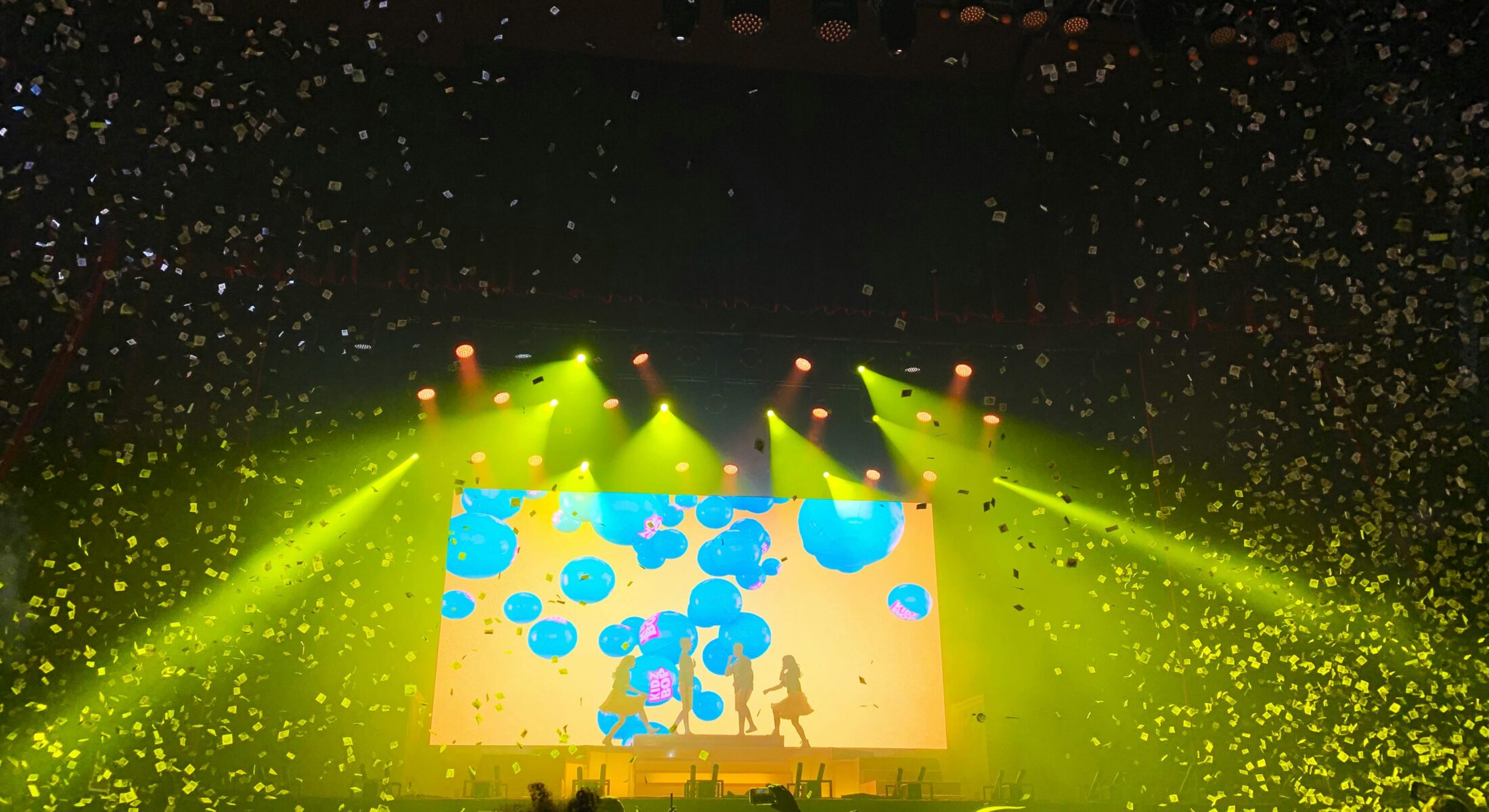 Colourful stadium concert scene with confetti, bright stage lights and a cheering crowd during a live music performance in Singapore
