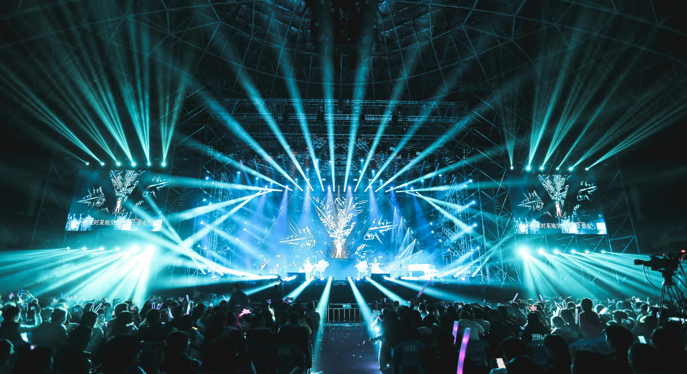 Stadium concert with dramatic blue stage lighting, large screens and a cheering crowd during a live music performance in Singapore