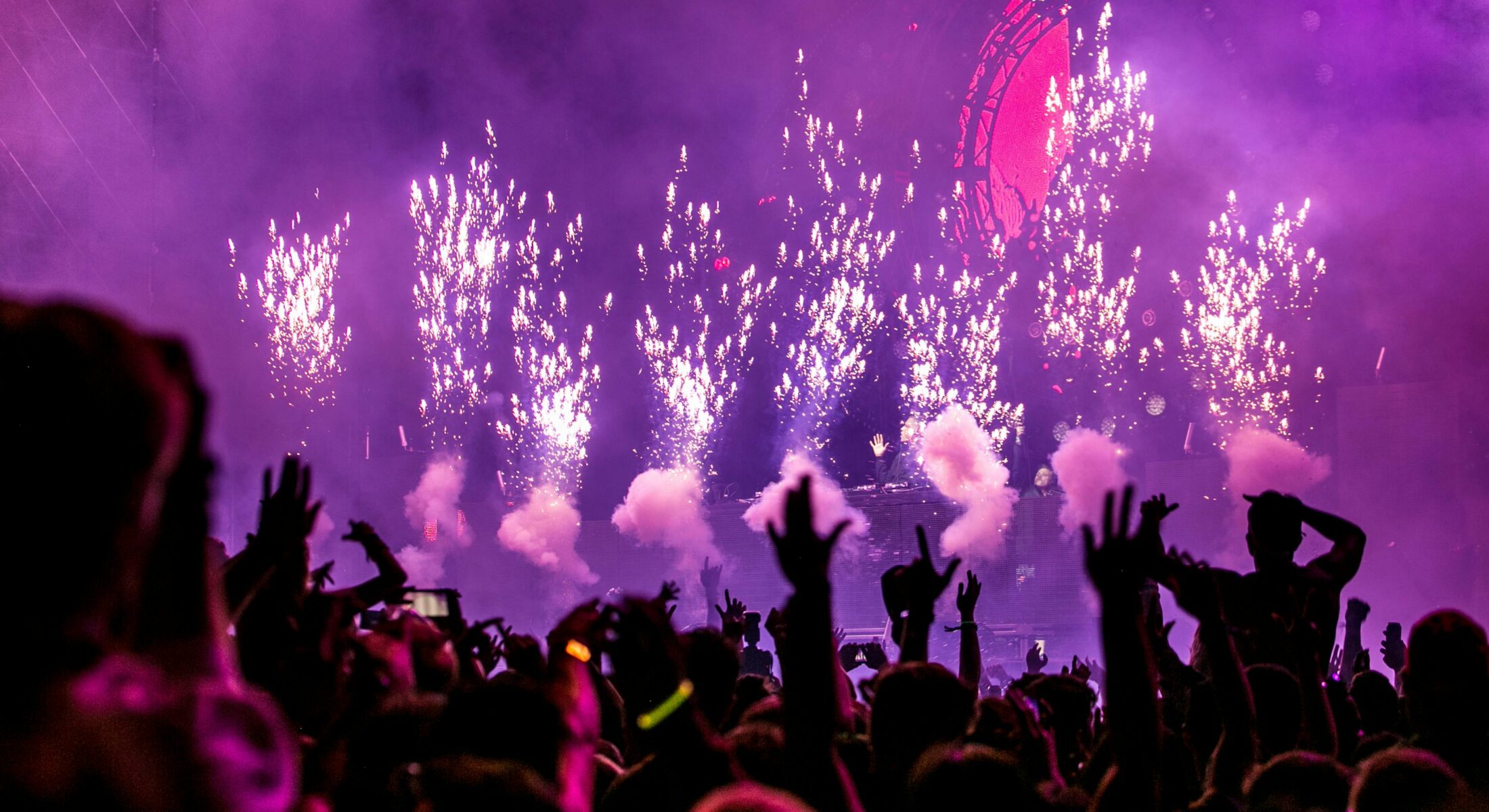 Energetic concert crowd with raised hands, vibrant purple stage lighting and pyrotechnic effects during a live music performance in Singapore