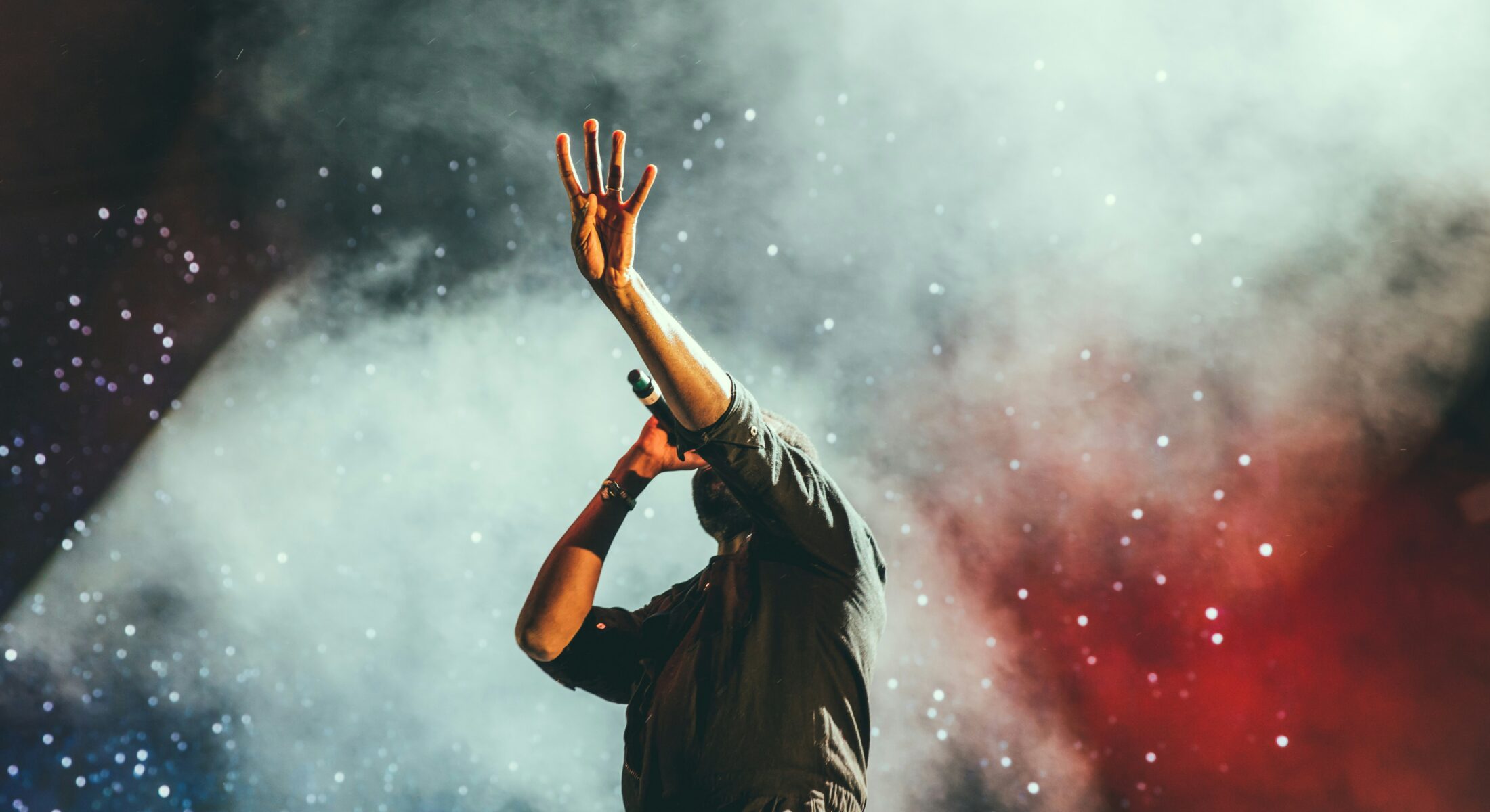 Performer holding a microphone during a live concert with dramatic smoke and stage lighting effects